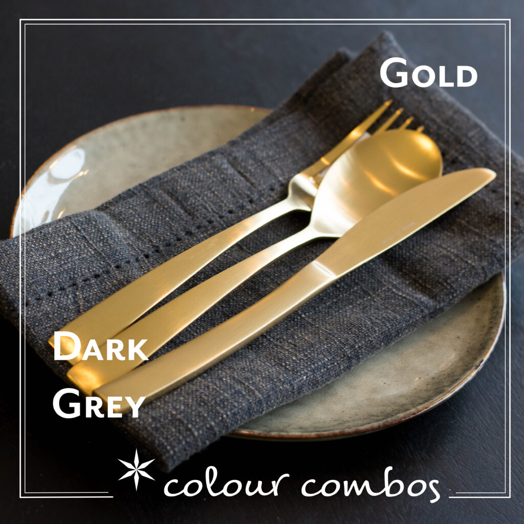 A gold fork, knife and spoon featured on a cold dark blue napkin and a slate grey plate.