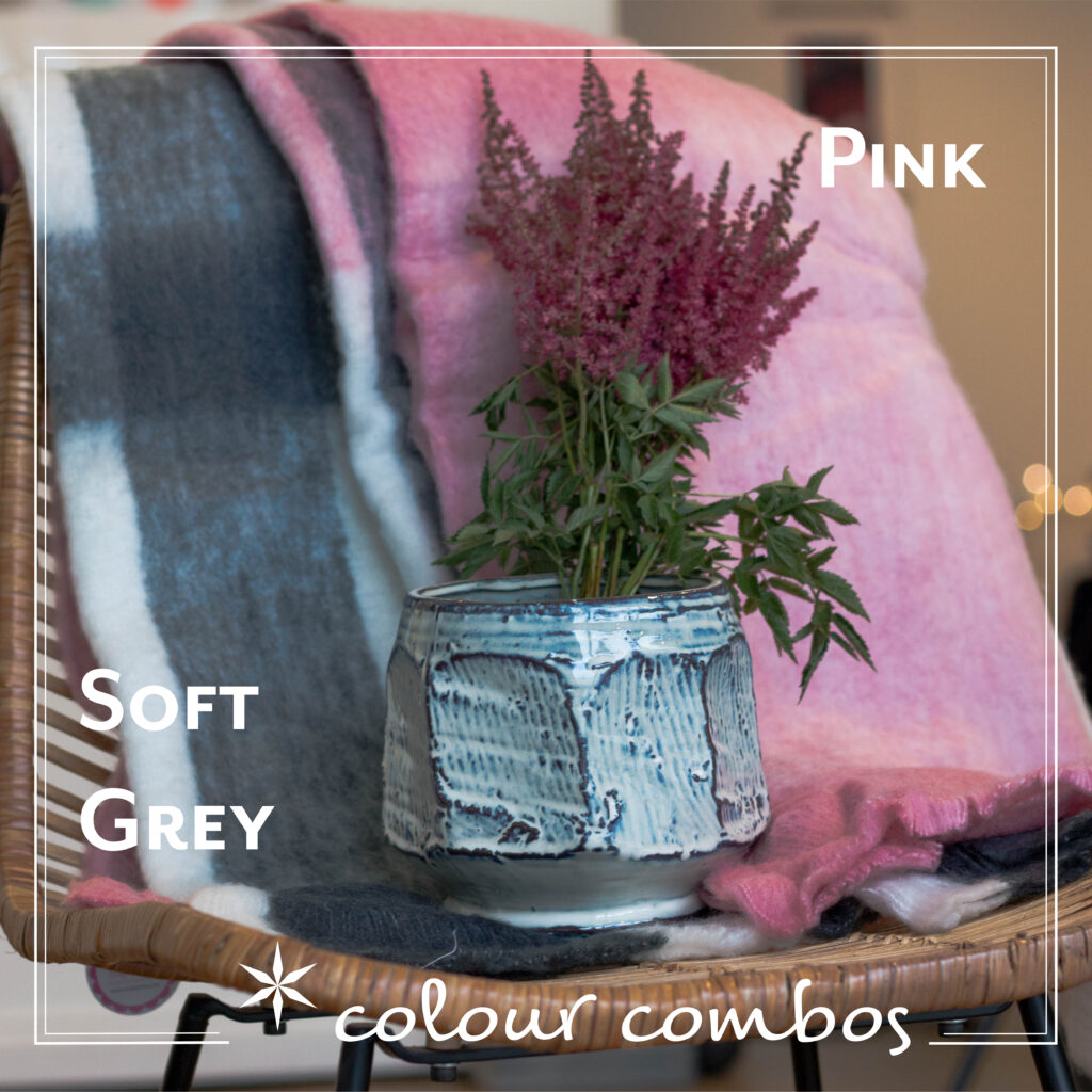 Beautiful blue natural textured vase with flowers in it featured on a pink and grey wool blanket on a chair.