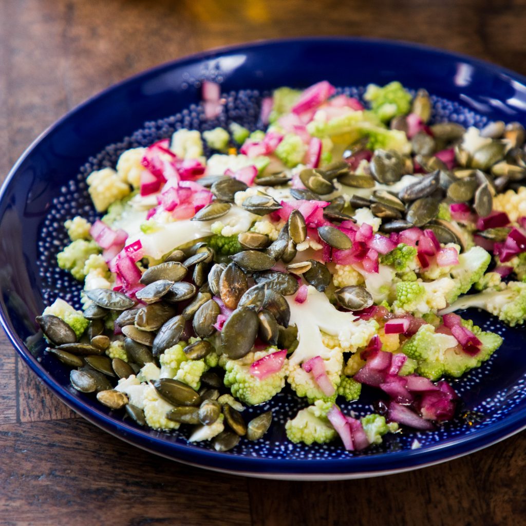 Image features a cauliflower and red onion pickle salad topped with pumpkin seeds on a blue plate.