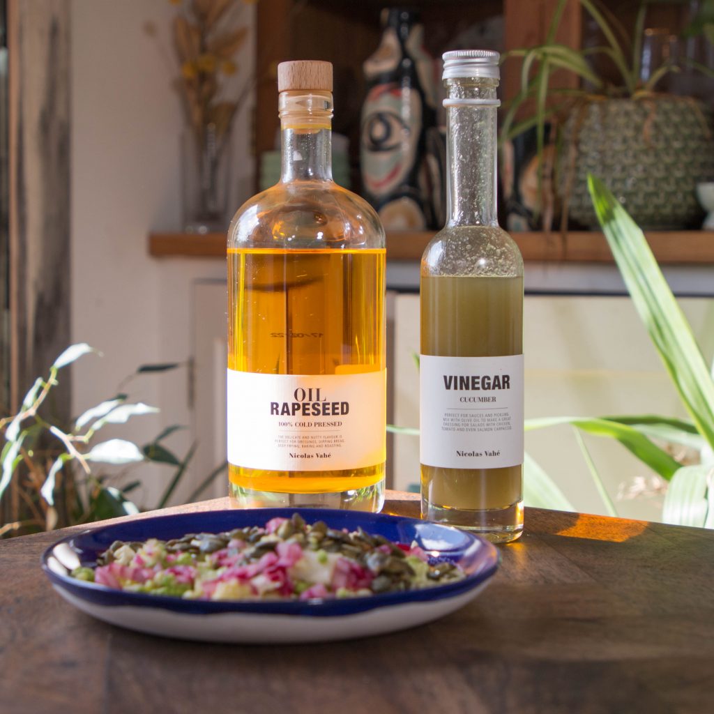 Image features a plate of salad in front of a bottle of rapeseed oil and a bottle of cucumber vinegar on a table.
