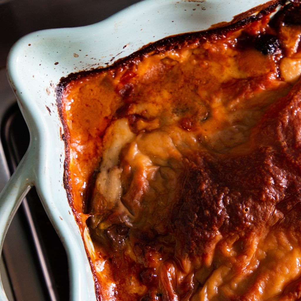 Image features a baked aubergine parmigiana inside a blue stoneware oven dish
