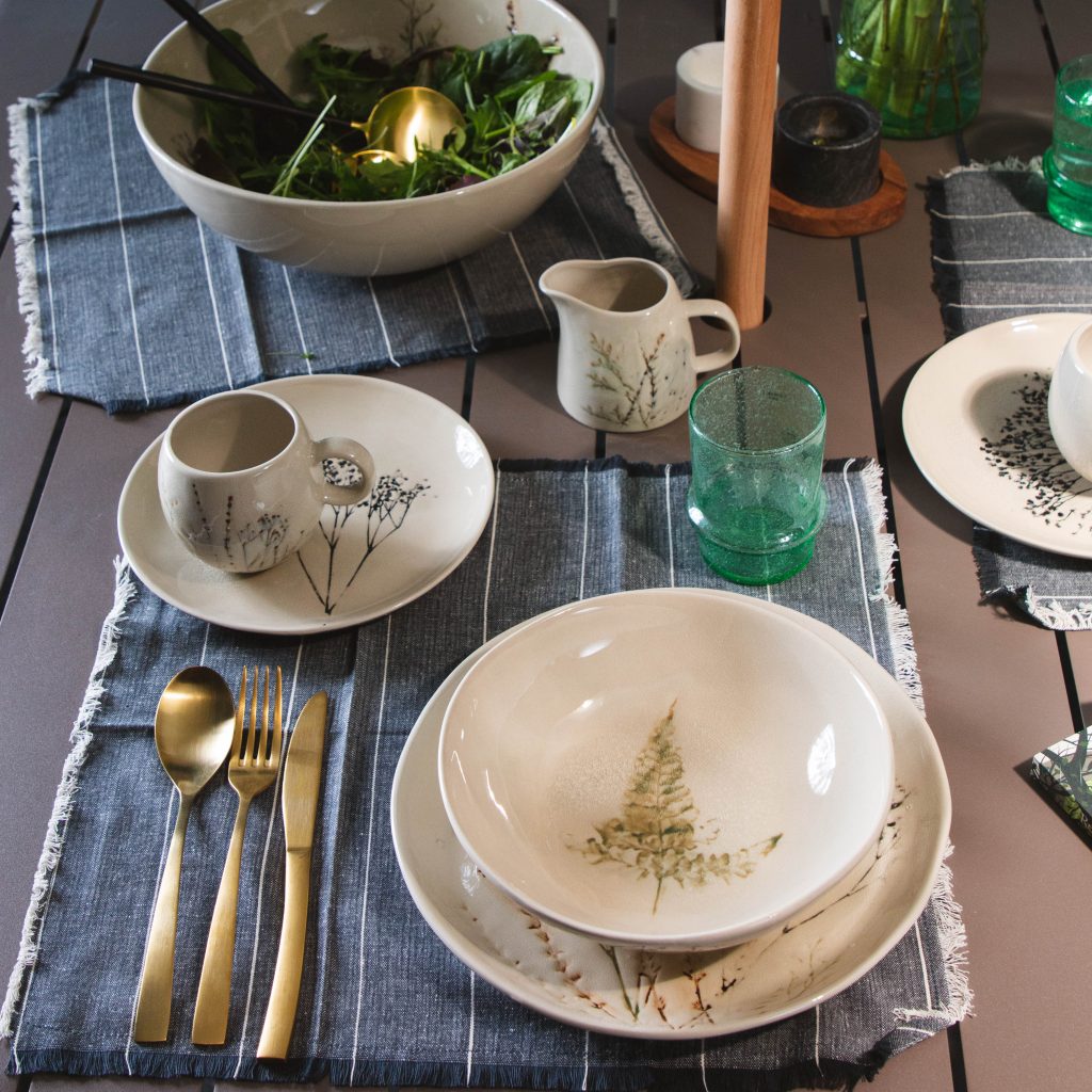 Image features the Bea tableware set from Bloomingville set up on a grey table with a blue napkin.